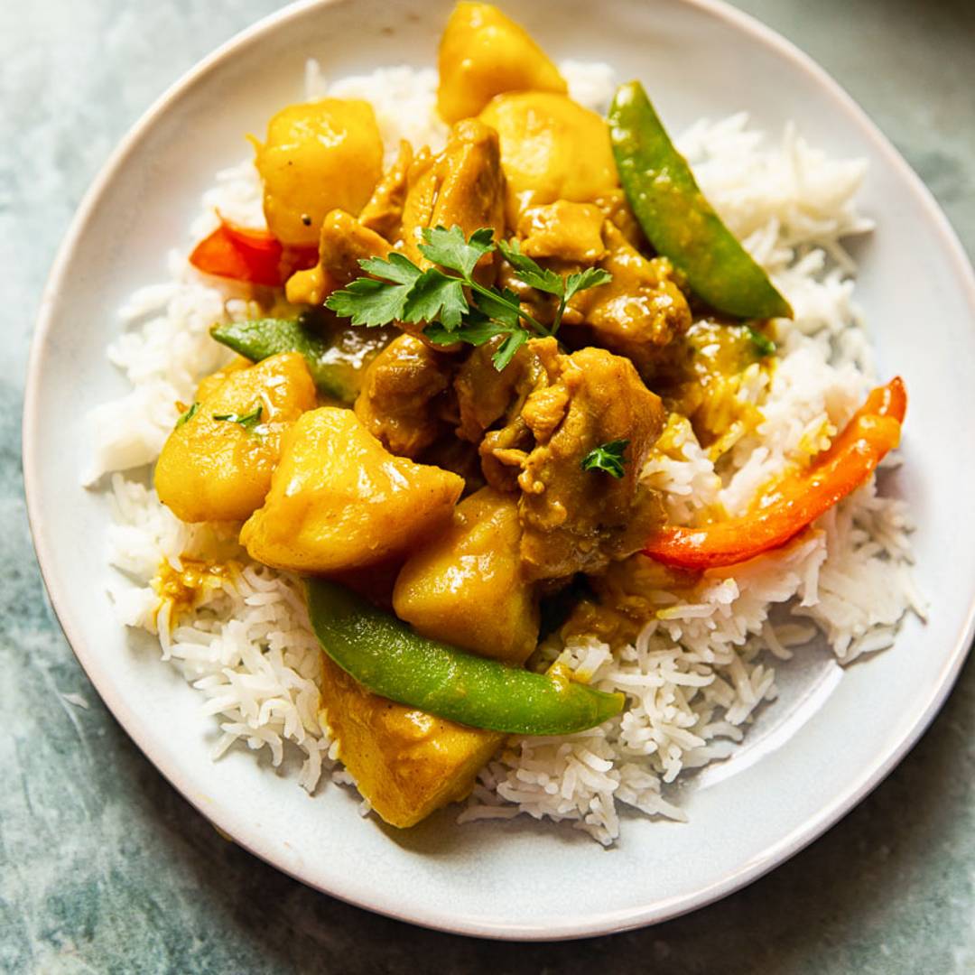 plate with white rice topped by a curry with chicken and vegetables
