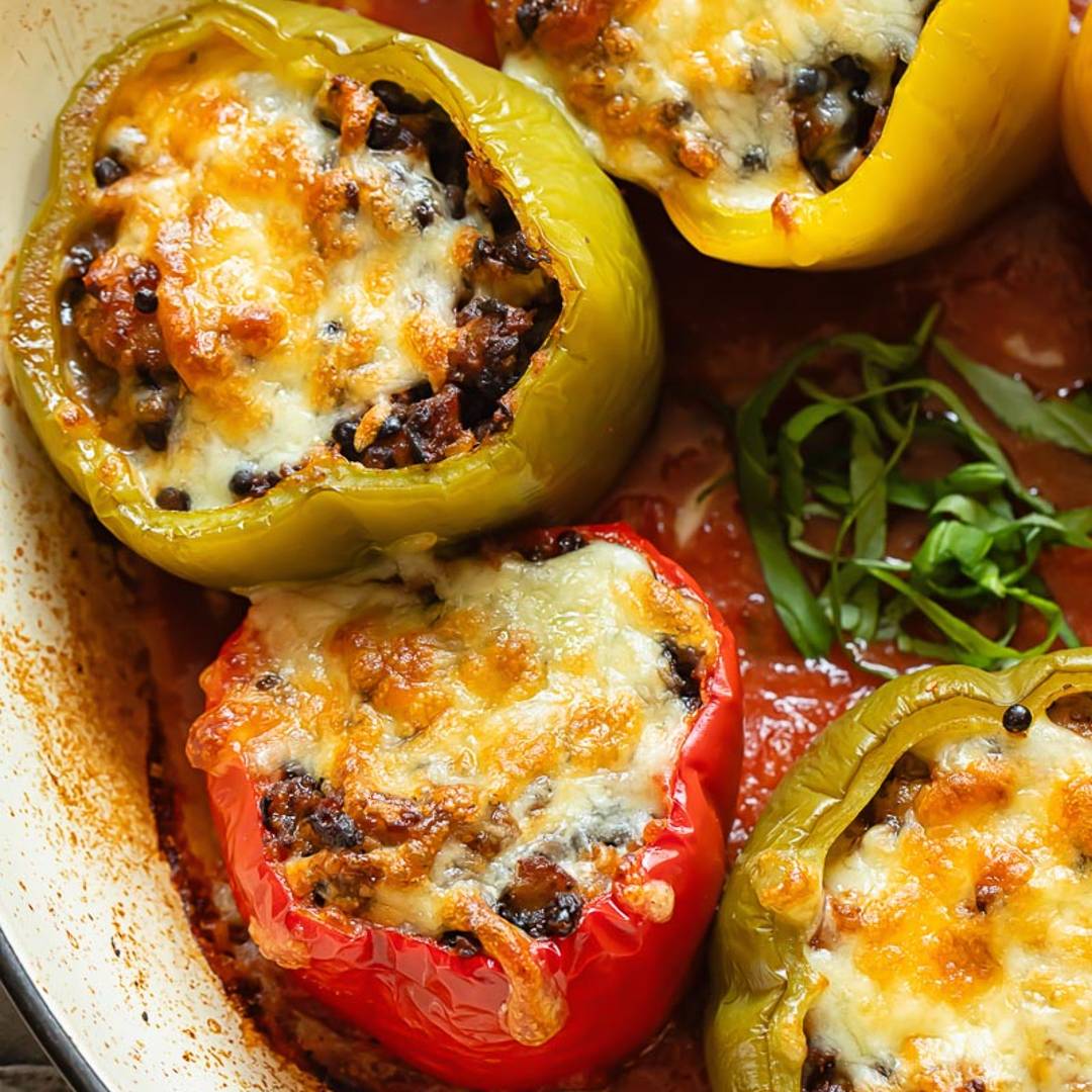 four stuffed peppers, topped with golden cheese, in a casserole dish on a layer of sauce