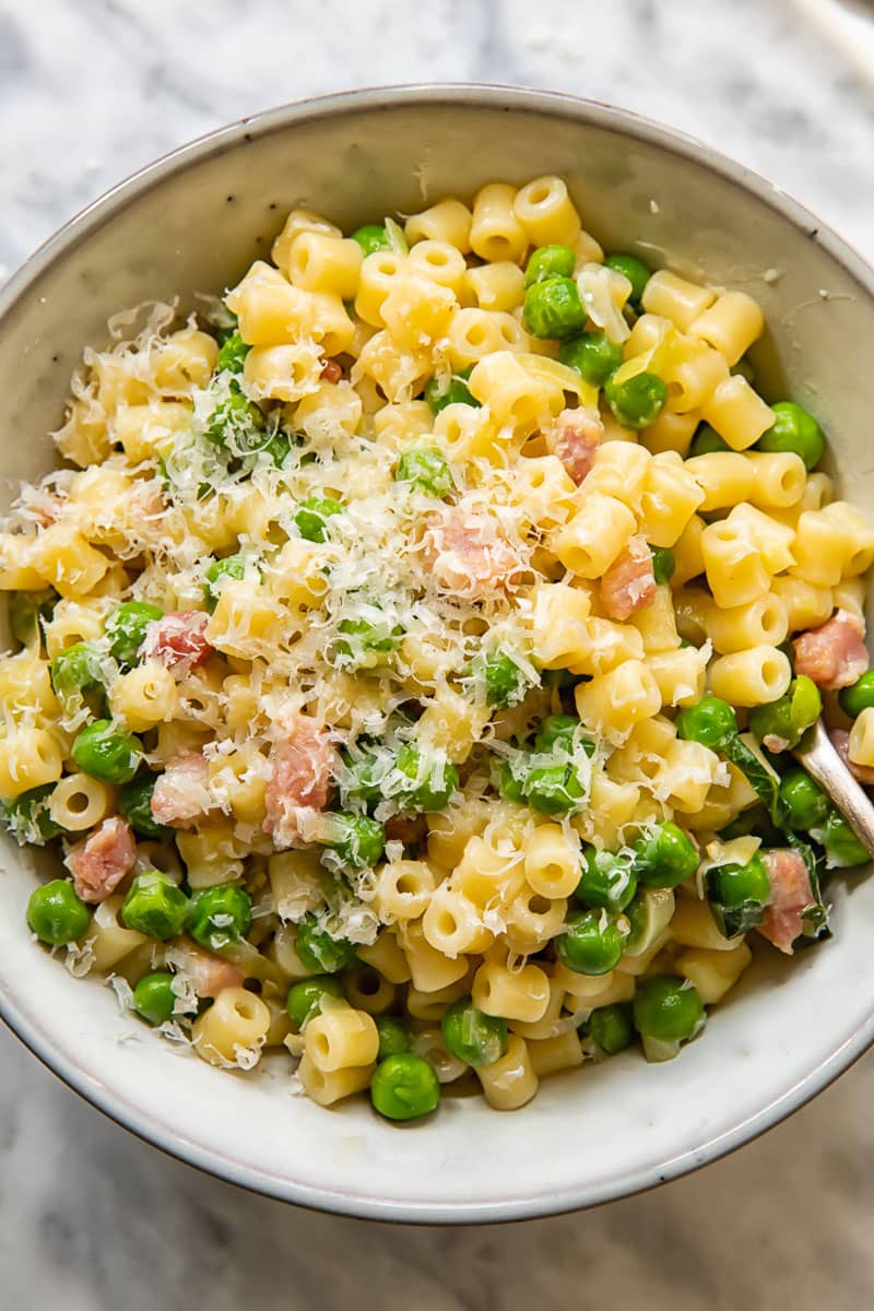 bowl of short pasta mixed with peas and ham and topped with shredded parmesan