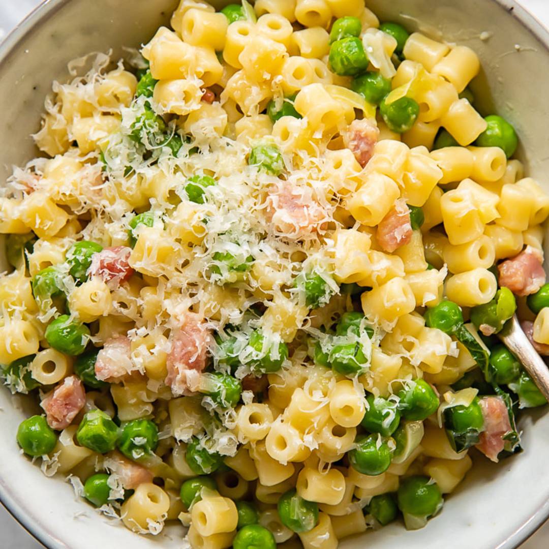 bowl of short pasta mixed with peas and ham and topped with shredded parmesan