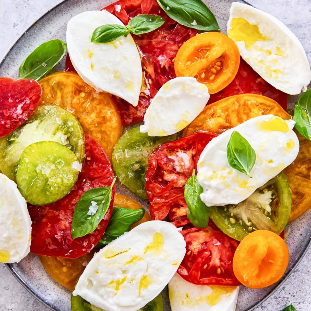 a grey plate with slices of tomato and fresh mozzarella, with basil leaves and olive oil