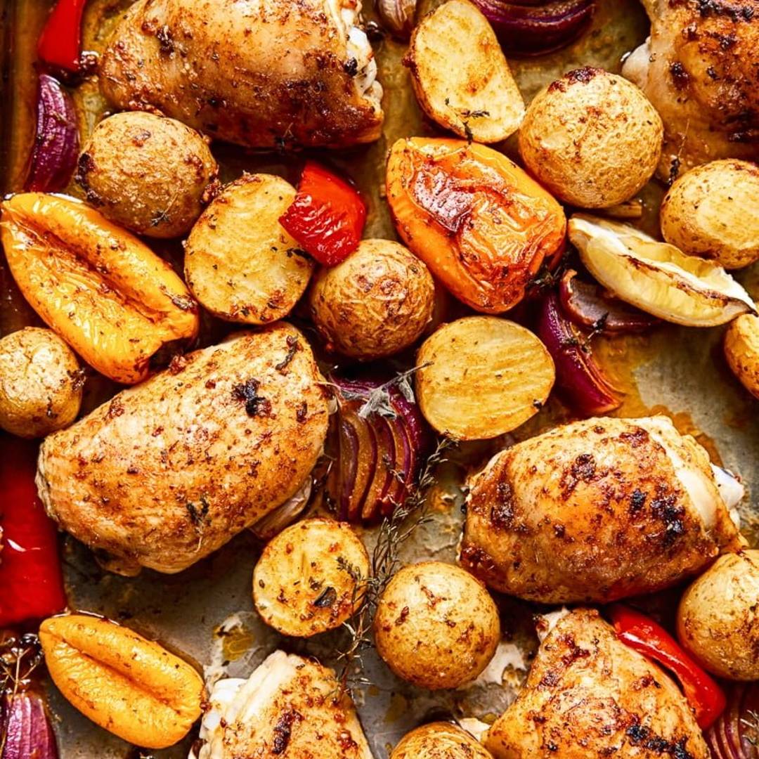 chicken thighs and potatoes on a baking sheet with onions and red peppers