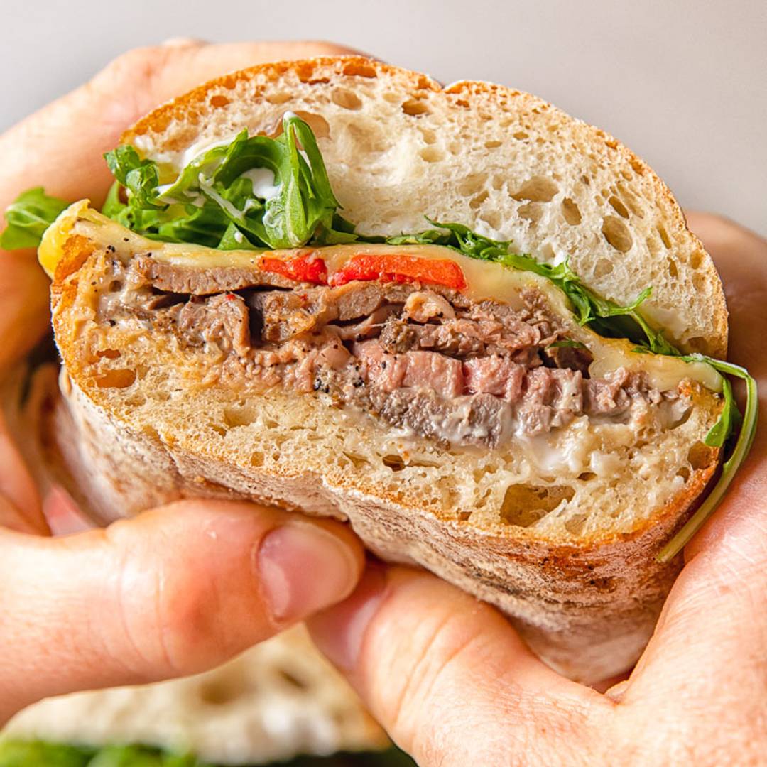 sandwich with roast beef being held by two hands 