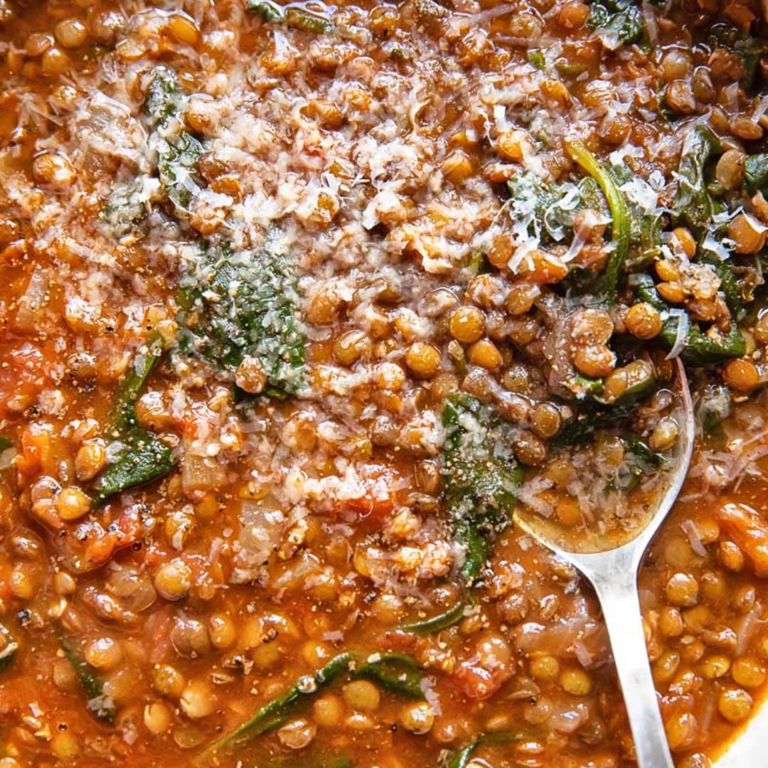 close up of a soup made with lentils and spinach in a red broth