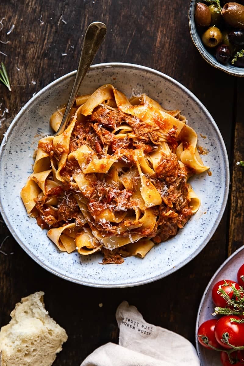 A bowl with pasta strands with a chunky meat sauce with a sprinkling of Parmesan cheese on a dark background