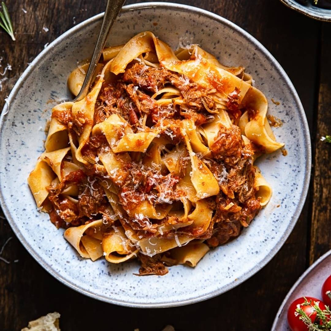A bowl with pasta strands with a chunky meat sauce with a sprinkling of Parmesan cheese on a dark background