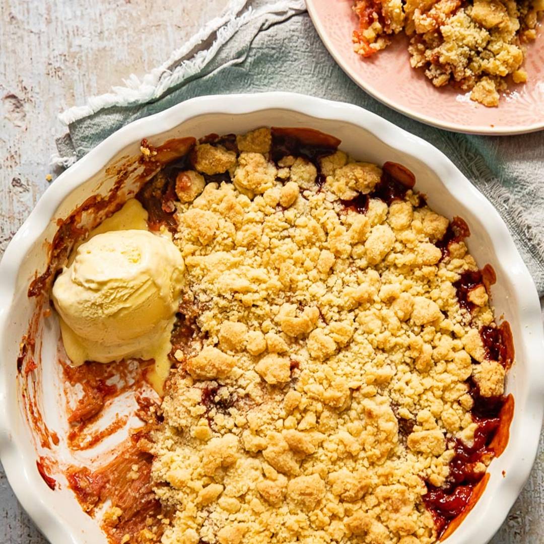 top down view of a pie dish with a crumble, with a scoop of ice cream, beside a small plate with a serving