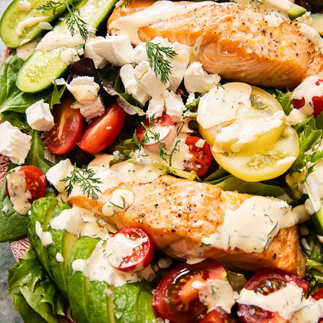 a mixed salad with a range of fresh ingredients, topped by salmon pieces and a creamy dressing