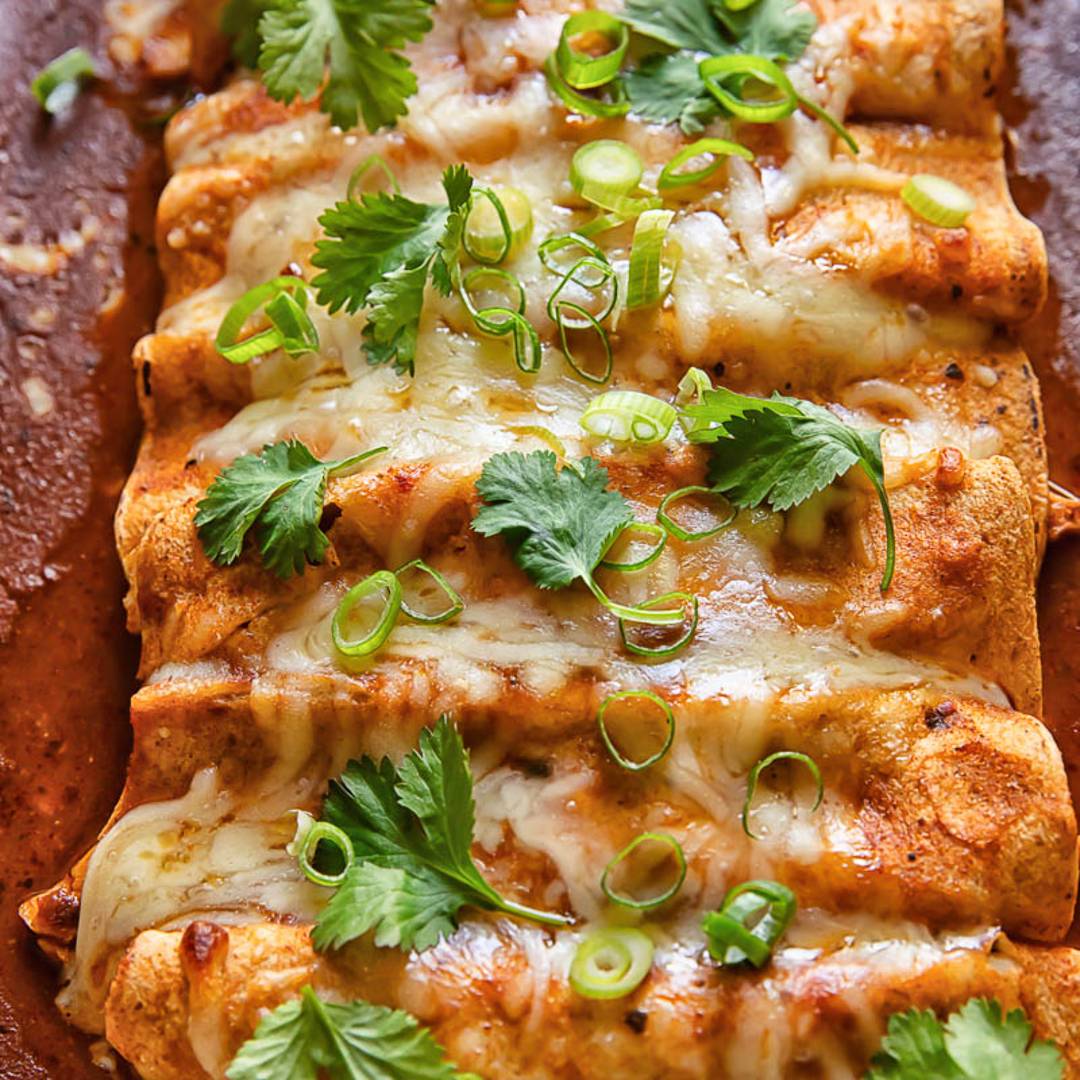 a row of baked tortilla wraps covered in cheese, cilantro and green onions