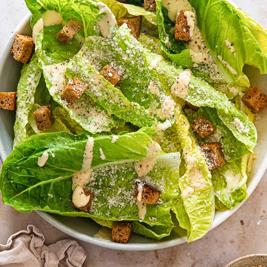 a bowl of caesar salad with creamy dressing and brown croutons