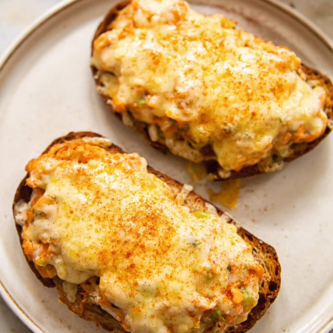 two open sandwiches on a plate with melted cheese