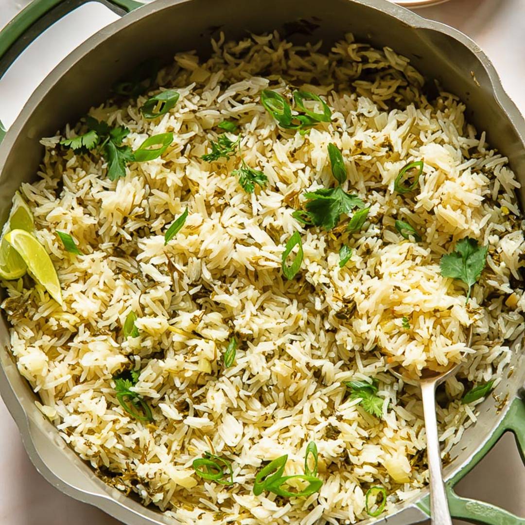pan of rice laced with herbs with two lime slices and a serving spoon