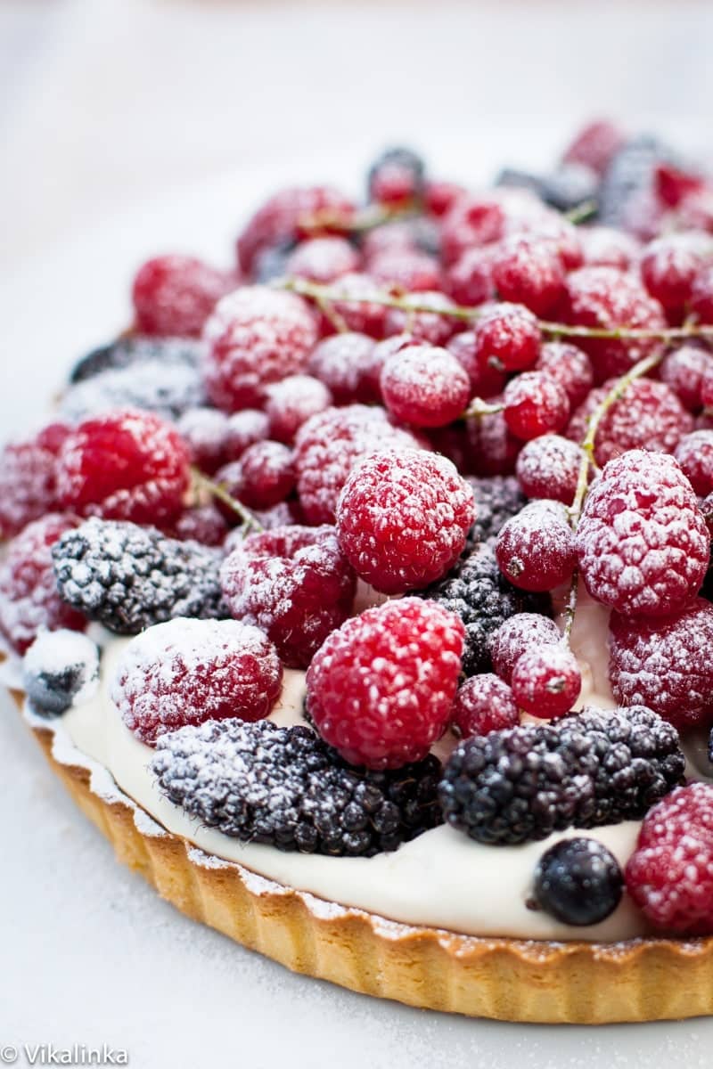 a close up of a tart covered with red and blue berries and a sprinkling of icing sugar