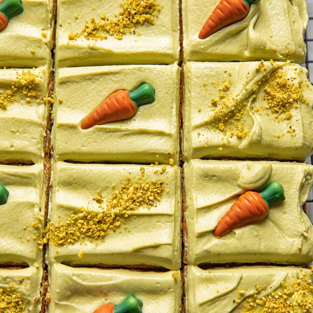 a sheet cake with green icing, decorated with carrots and chopped pistachios