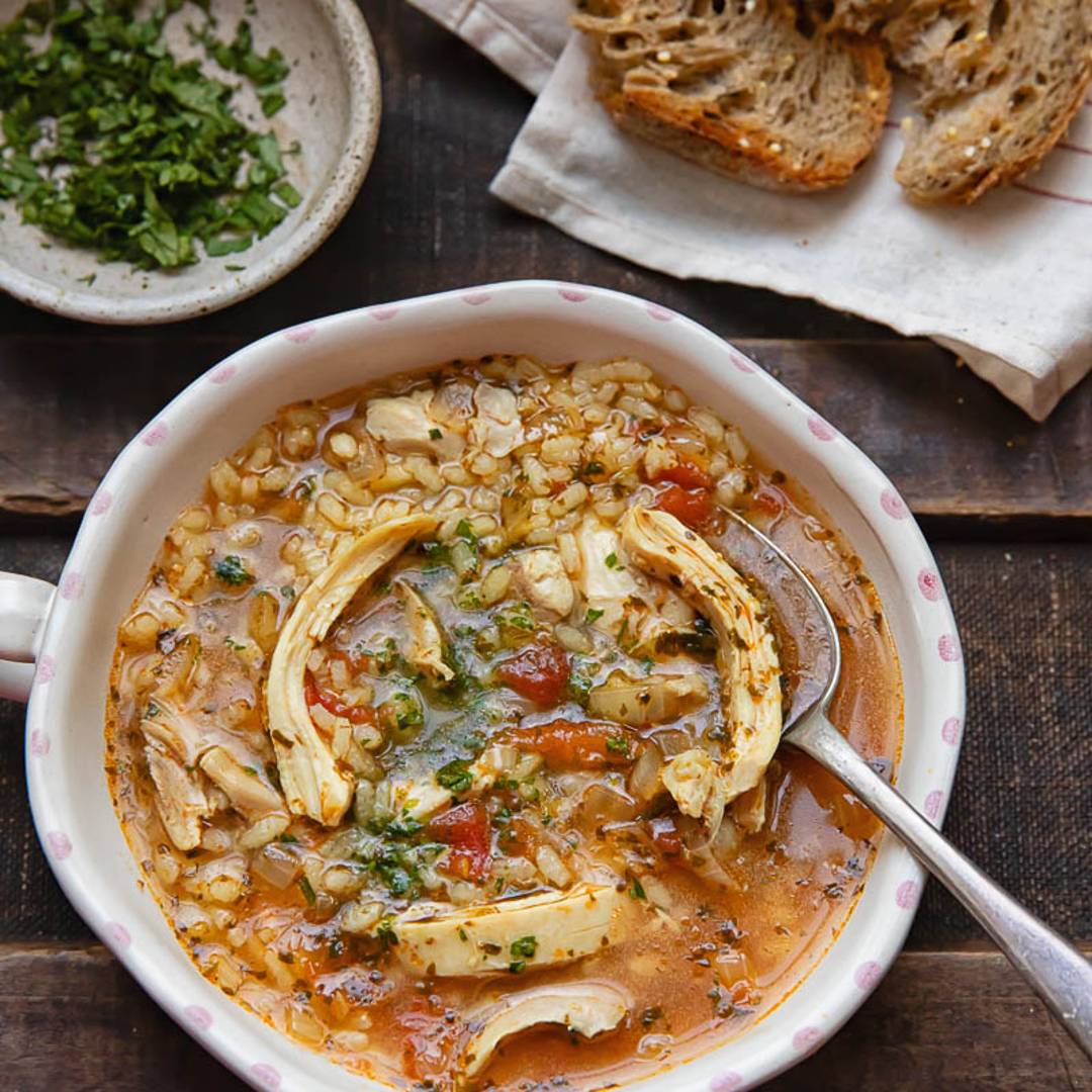 bowl of chicken soup with grains and vegetables with bread and herbs