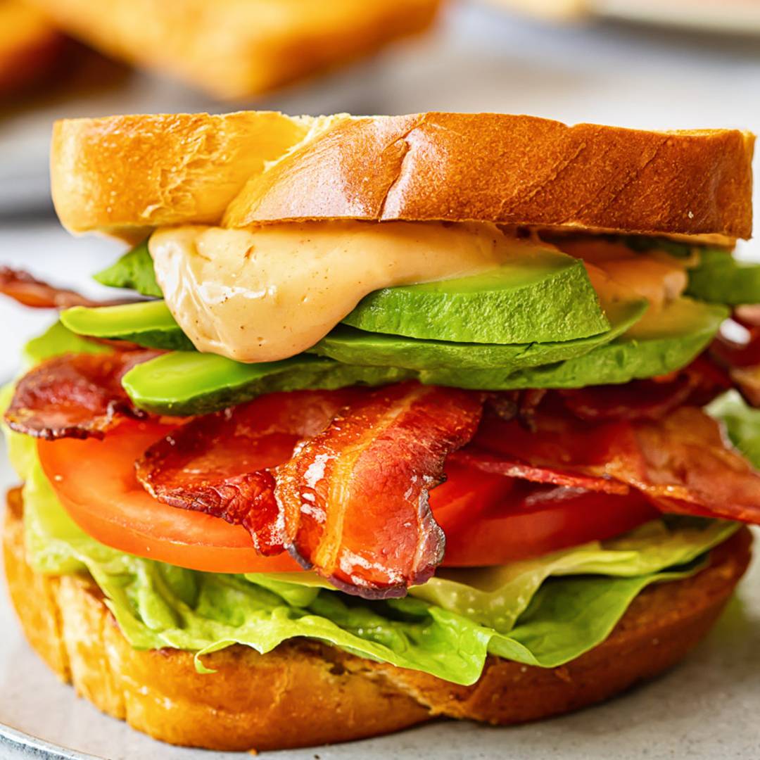 sandwich on a blue plate, made with lettuce, bacon, tomato and a sauce
