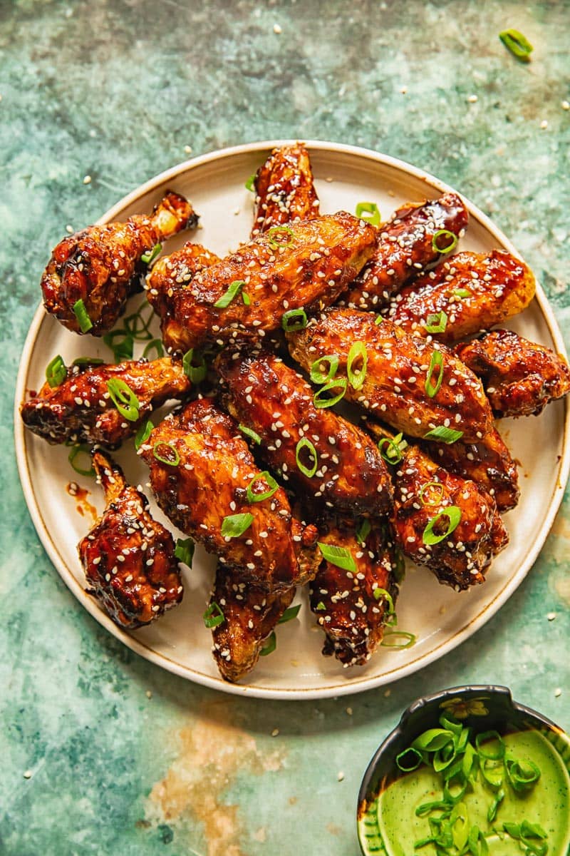 white plate on a marble background with glazed chicken wings covered by a sprinkling of green onions