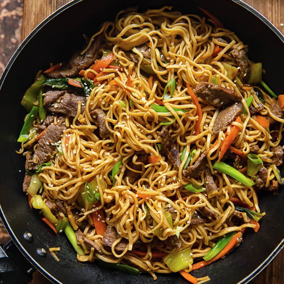 top down of a wok with stir fried noodles against a wooden background