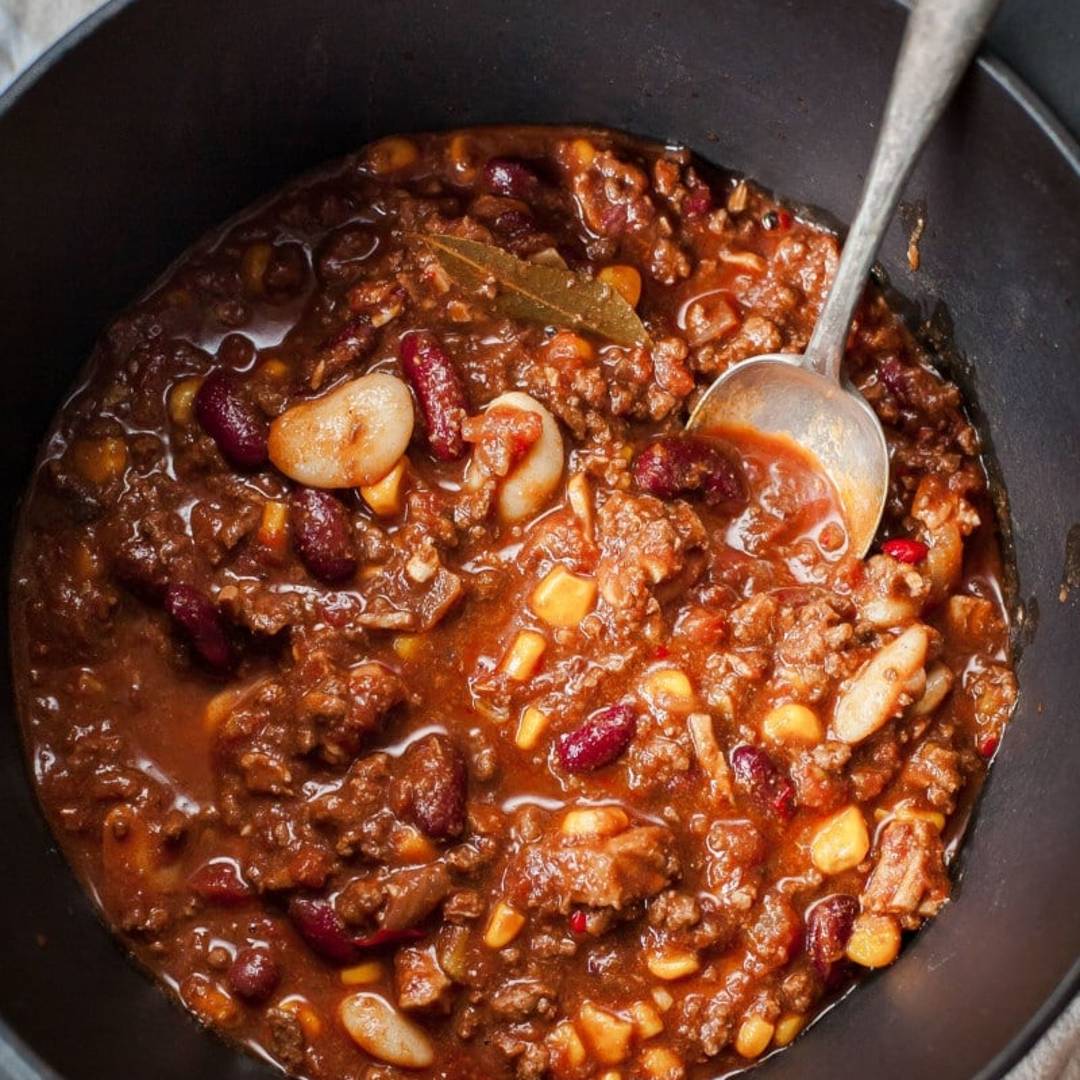 a pot of chili with beans, meat and corn, plus a serving spoon inserted
