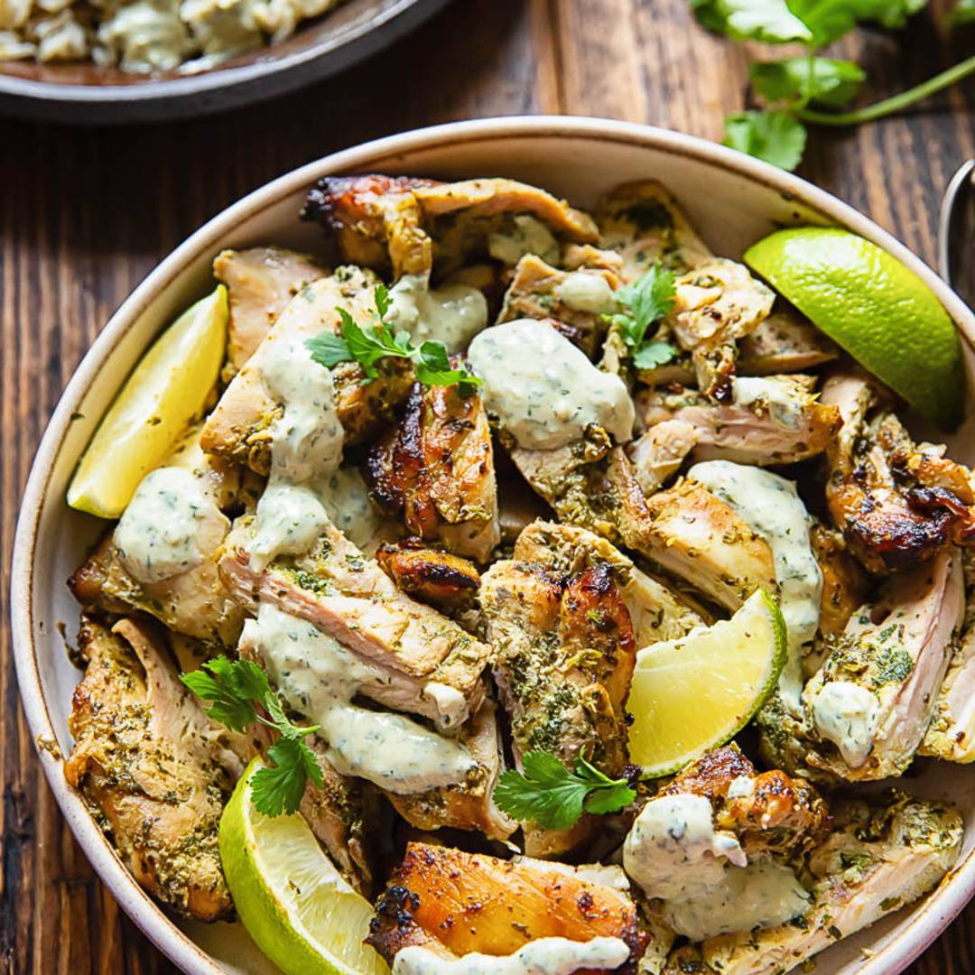 a shallow bowl on a wooden table, with pieces of chicken, slices of lime and a drizzle of a creamy sauce