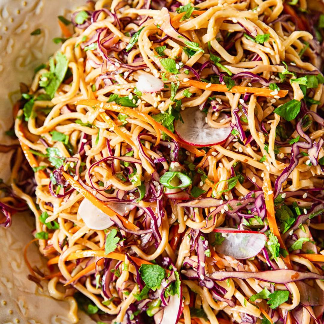 a bowl with long noodles mixed with sliced cabbage, radishes and green herbs