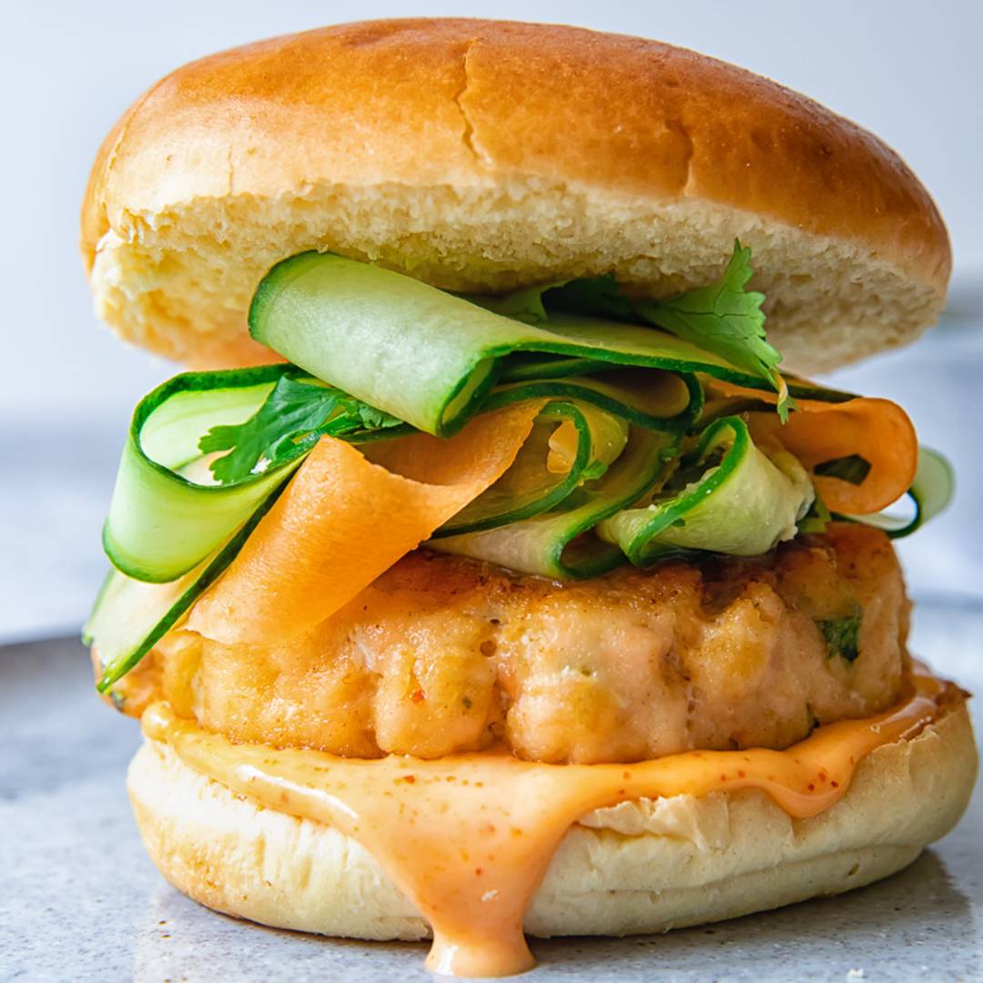 side view of a burger with salmon patty and thinly sliced cucumber and carrot