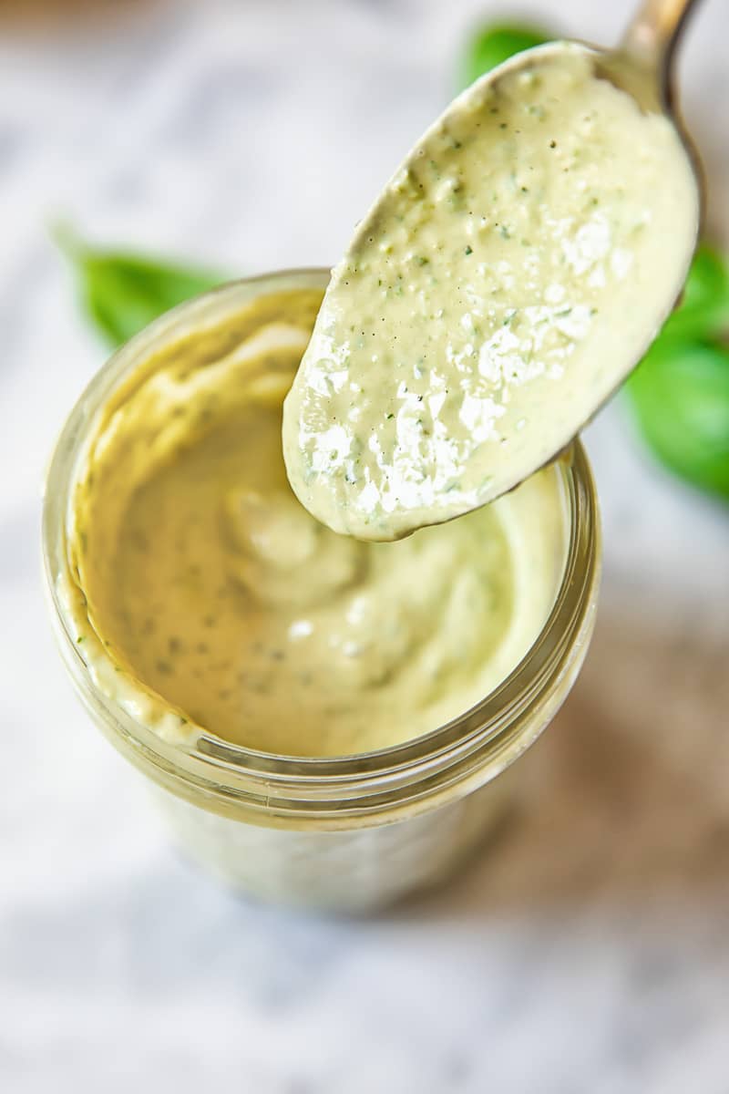 top down view of a jam jar with a creamy light green dressing, with a spoon removing a portion