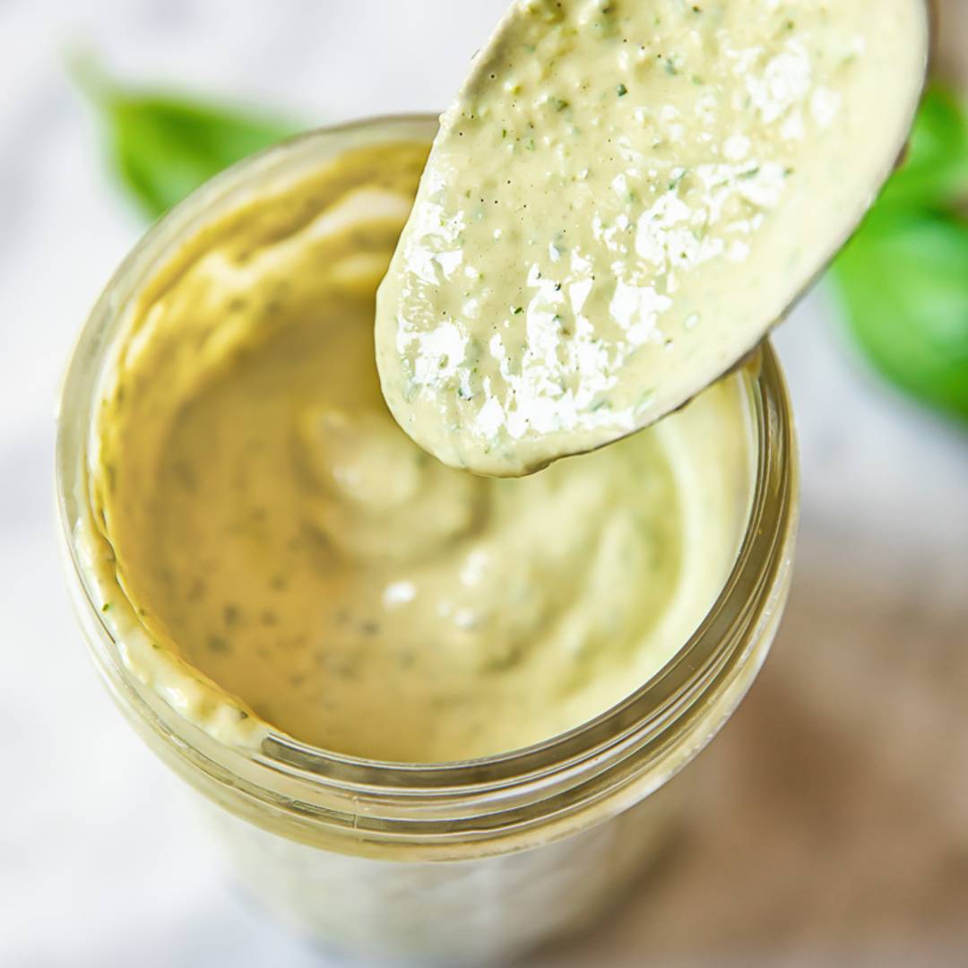 top down view of a jam jar with a creamy light green dressing, with a spoon removing a portion