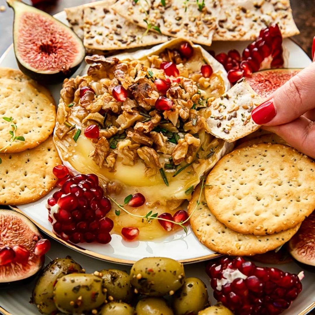 a melty brie topped with walnuts and pomegranate seeds, and surrounded by figs, crackers and olives