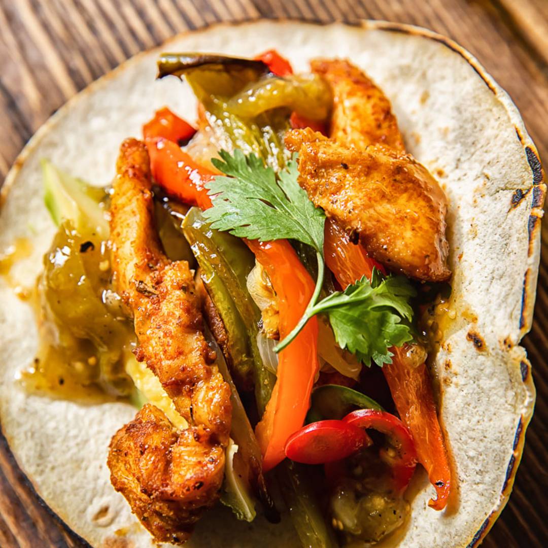 a tortilla with chicken pieces, sliced peppers and cilantro on a wooden background