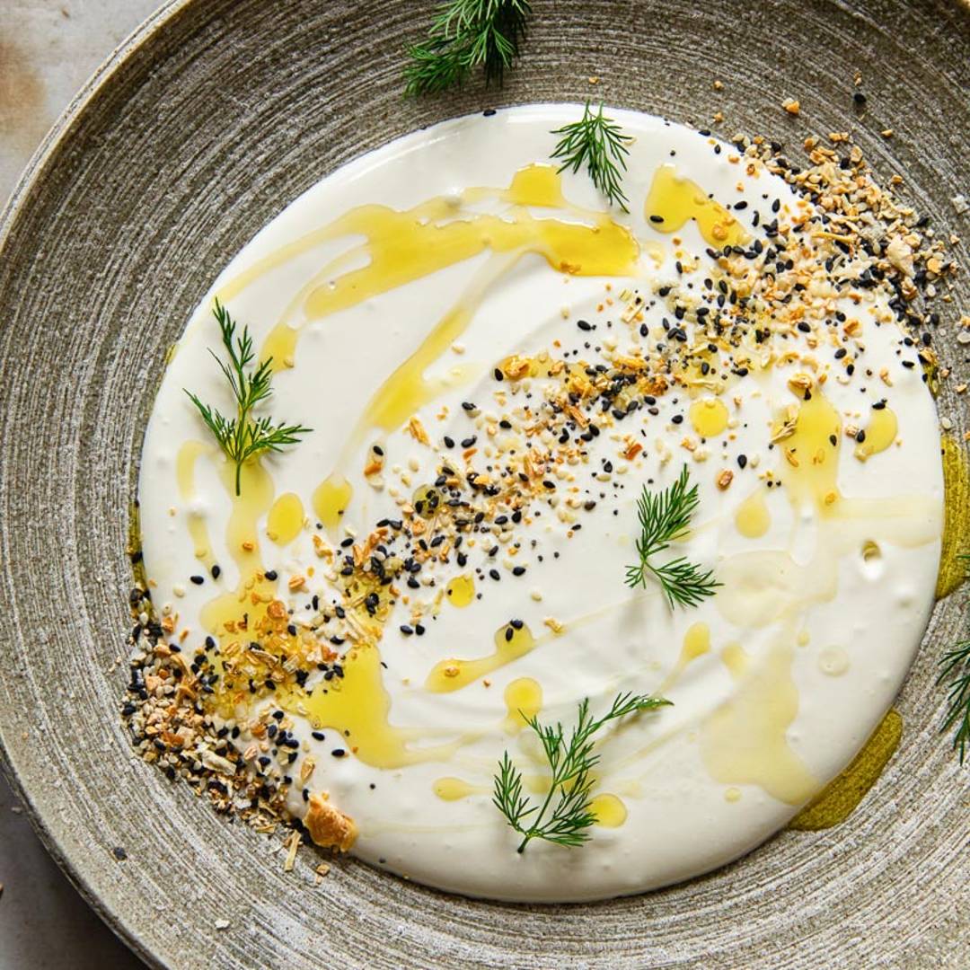 a plate with a white dip topped with everything bagel seasoning and dill
