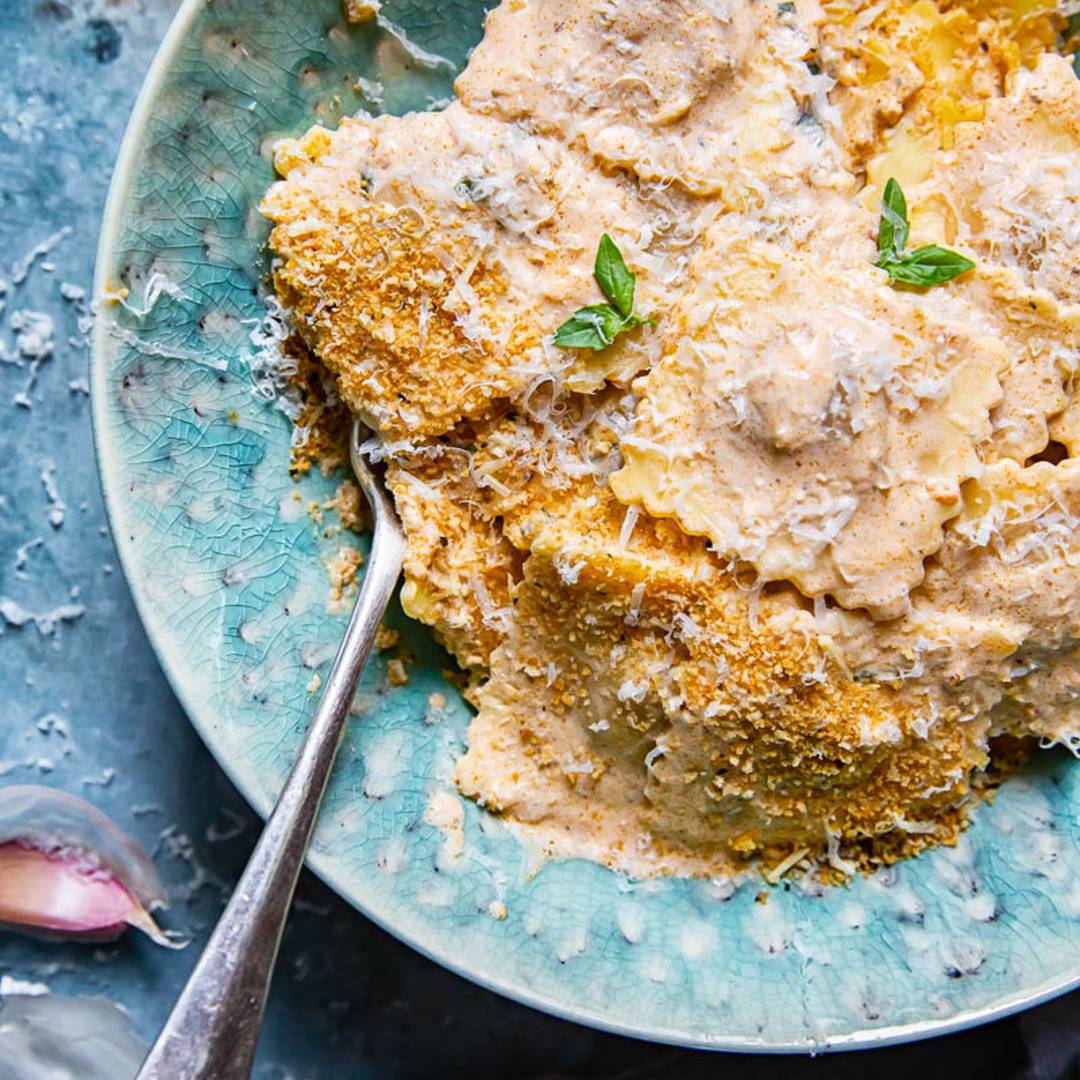 a green bowl holding ravioli in a creamy sauce and topped with shaved Parmesan cheese.