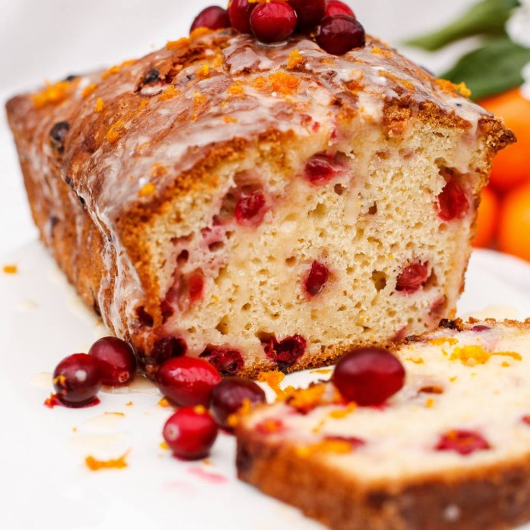 a loaf of bread cut open to reveal the inside, with a piece lying in front and scattering of cranberries