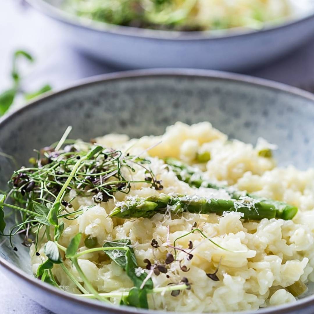 a blue bowl of risotto with asparagus and micro herbs on top