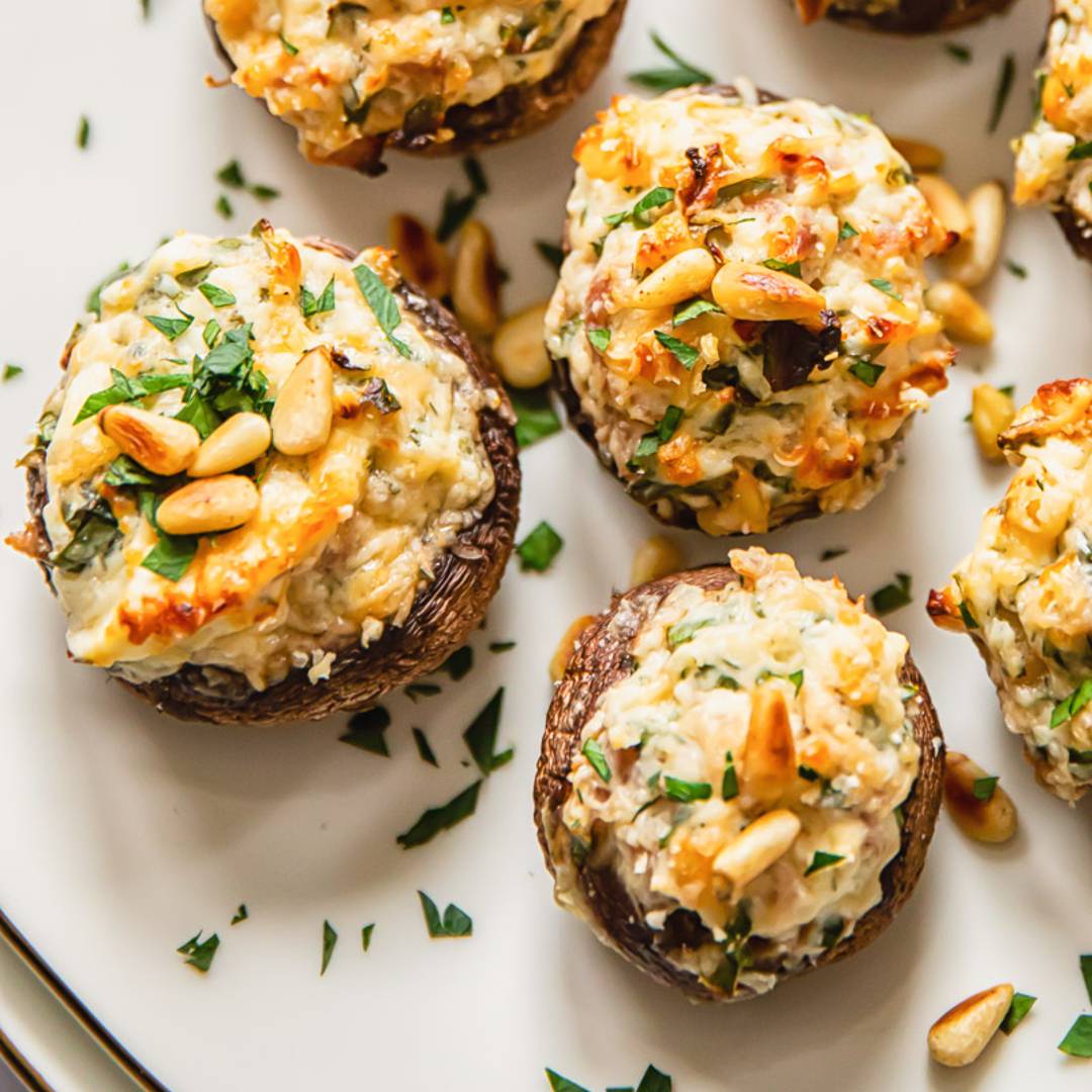 stuffed mushrooms on a plate topped with pine nuts and herbs