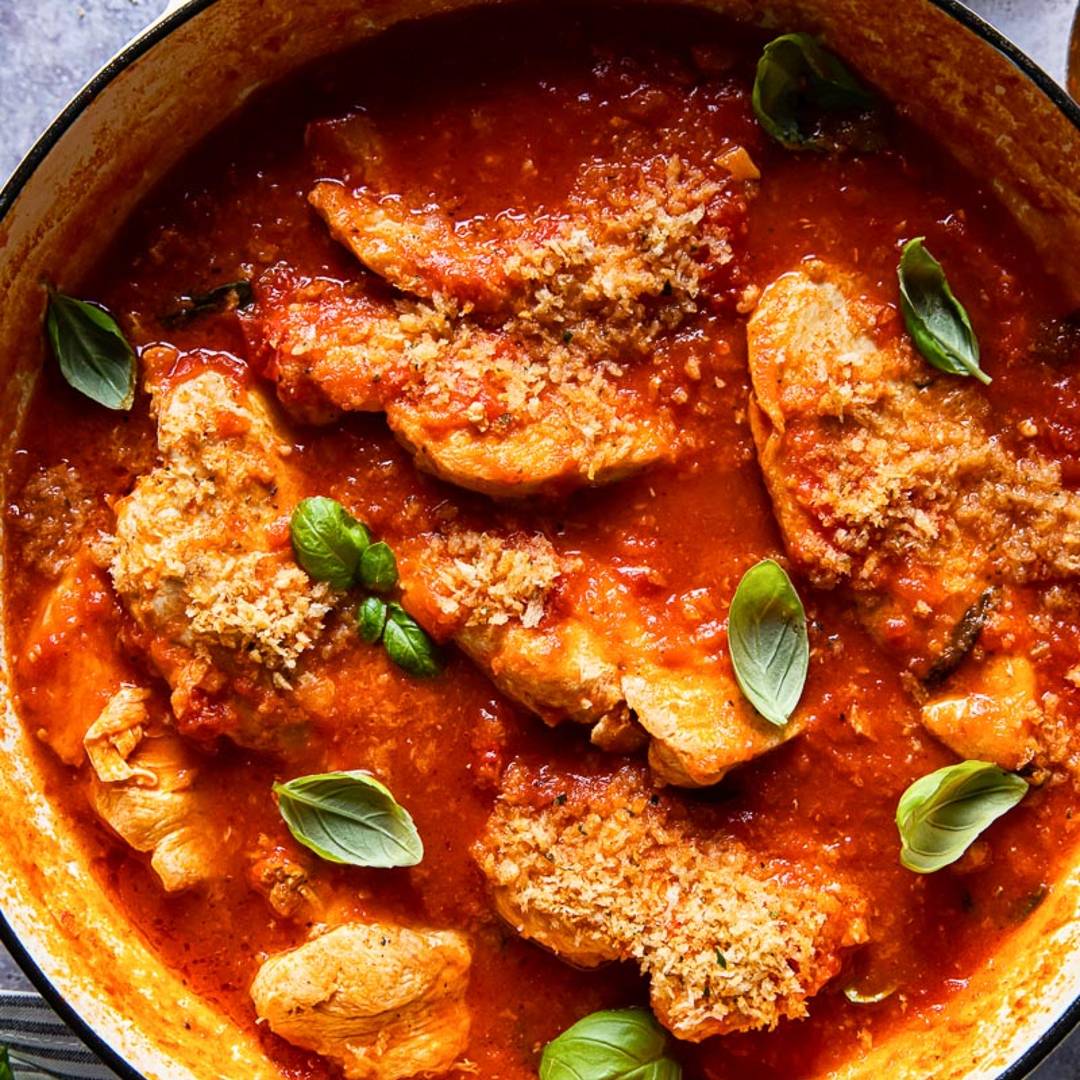 pan with chicken in a red sauce topped with basil leaves