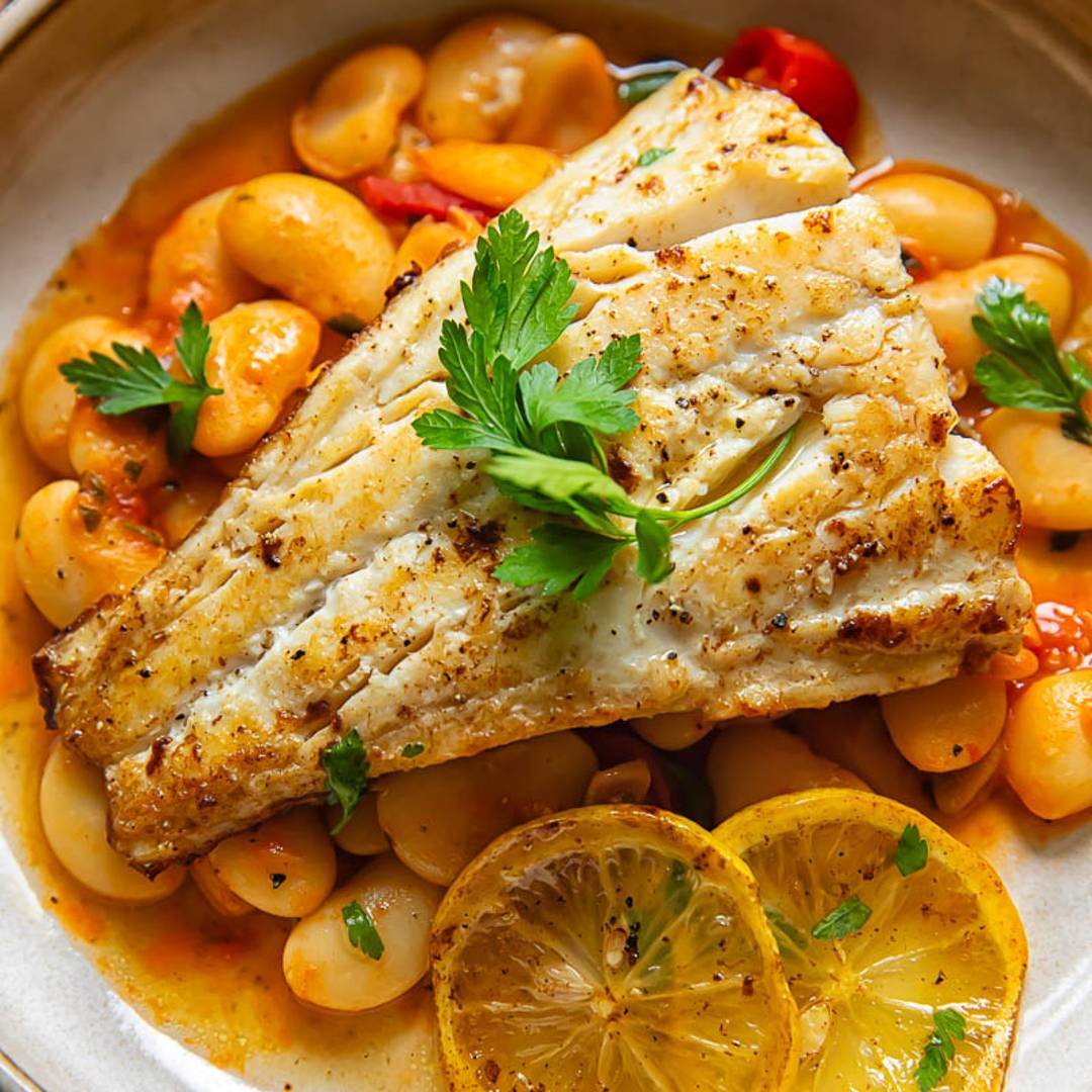 piece of cod in a shallow bowl topping white beans, with added lemon slices and parsley