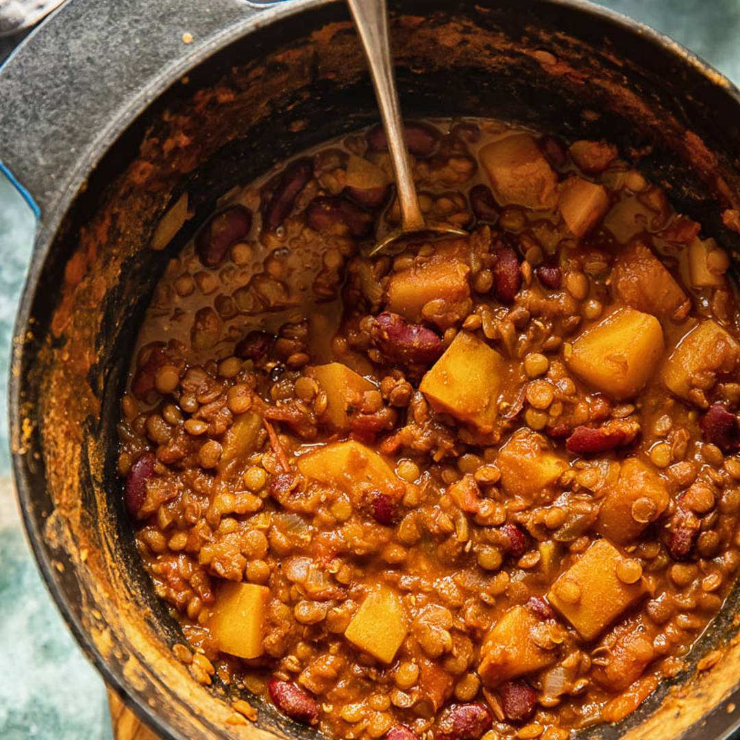 a pot full of a chili made of squash and lentils with a serving spoon