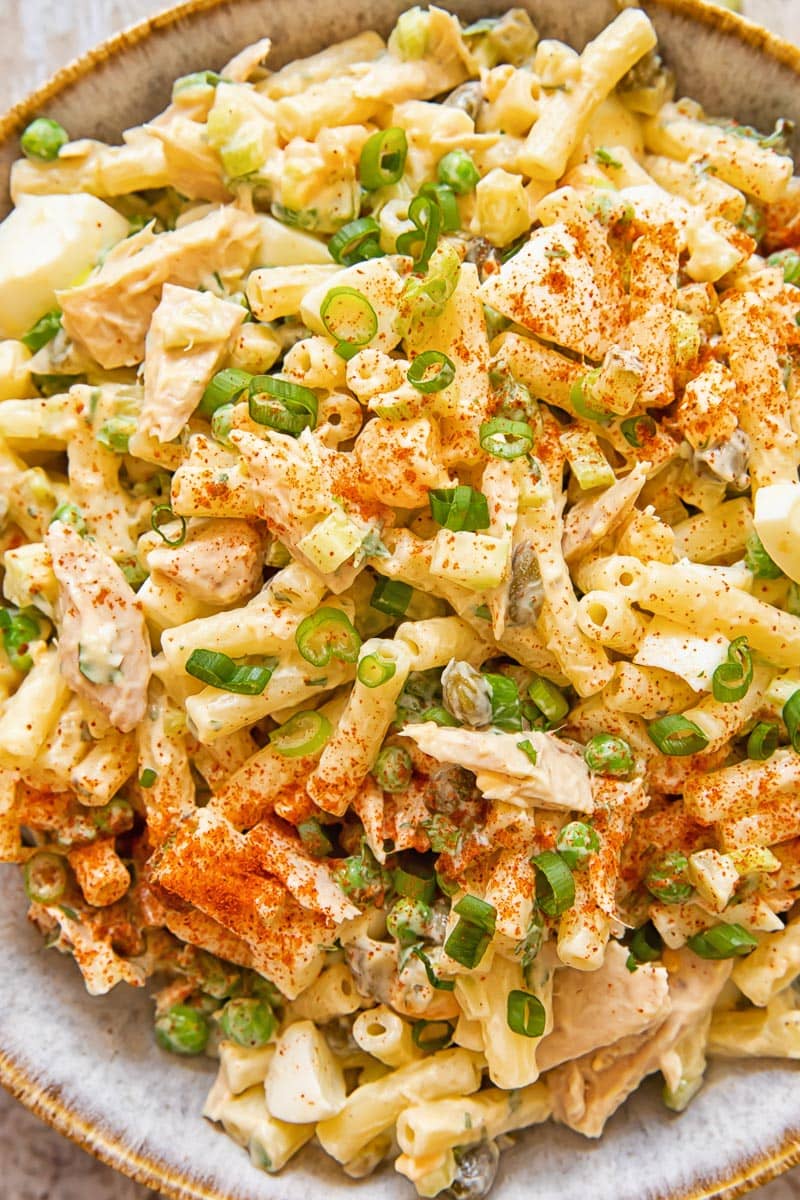 bowl of tuna salad with macaroni topped with sliced green onions and a sprinkling of red spice