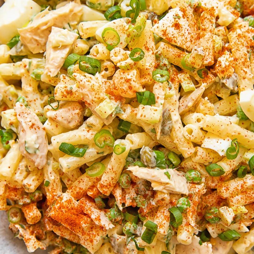 bowl of tuna salad with macaroni topped with sliced green onions and a sprinkling of red spice