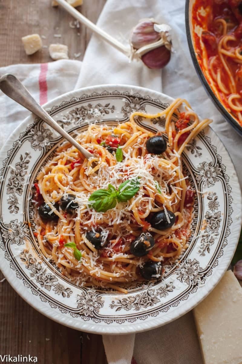 A rustic bowl of spaghetti in a red sauce with olives and grated cheese.