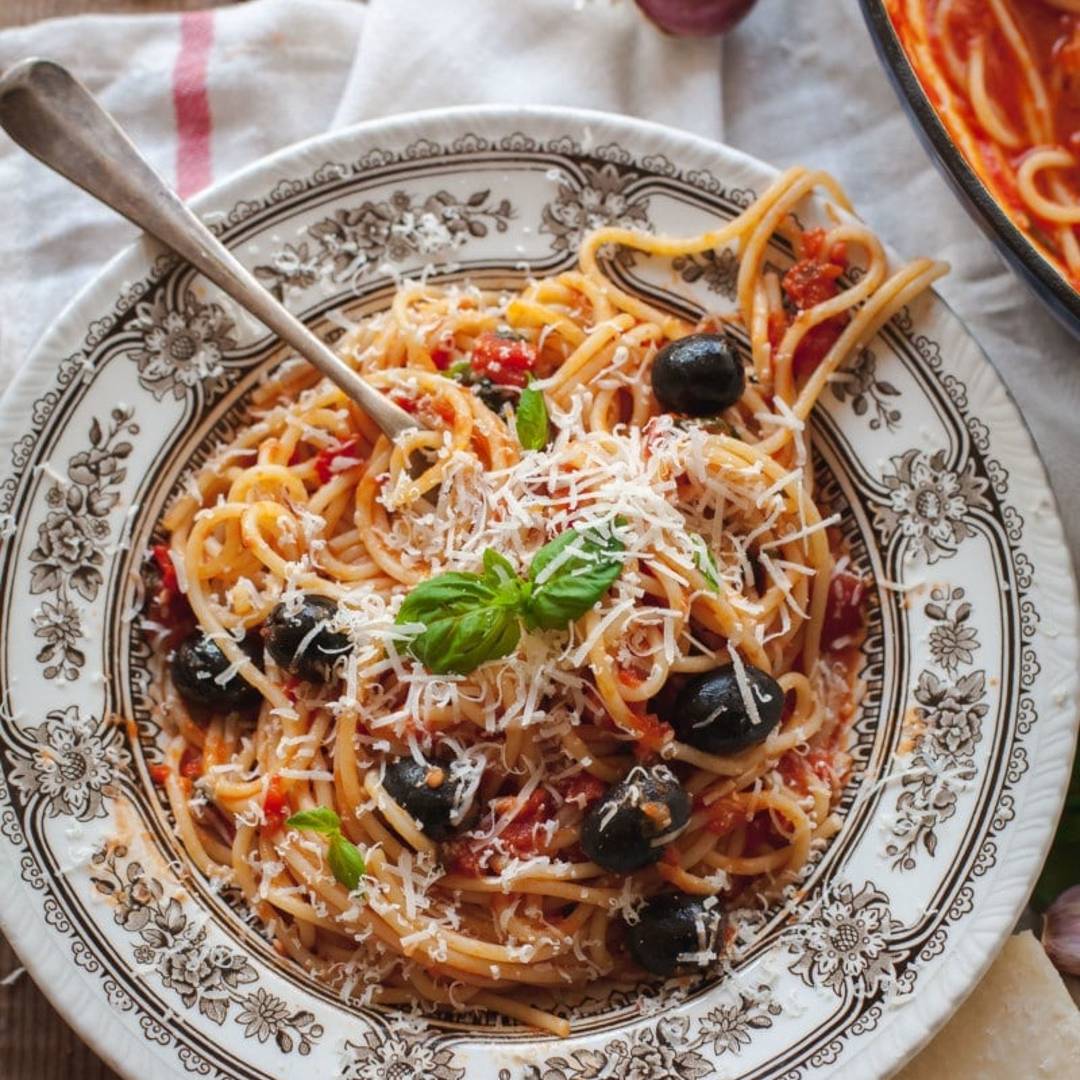 A rustic bowl of spaghetti in a red sauce with olives and grated cheese.