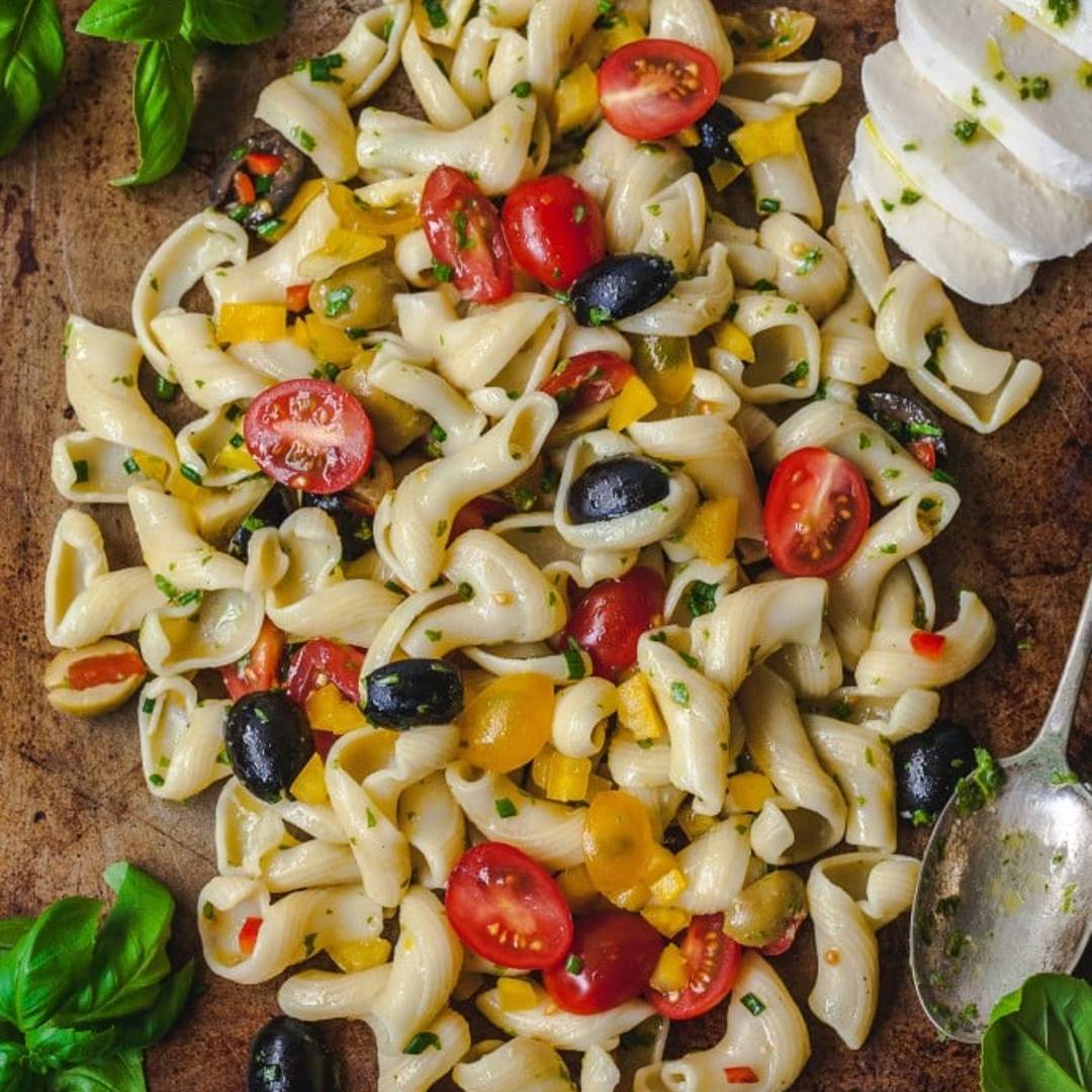 pasta salad with tomatoes and olives prominent on a rustic background