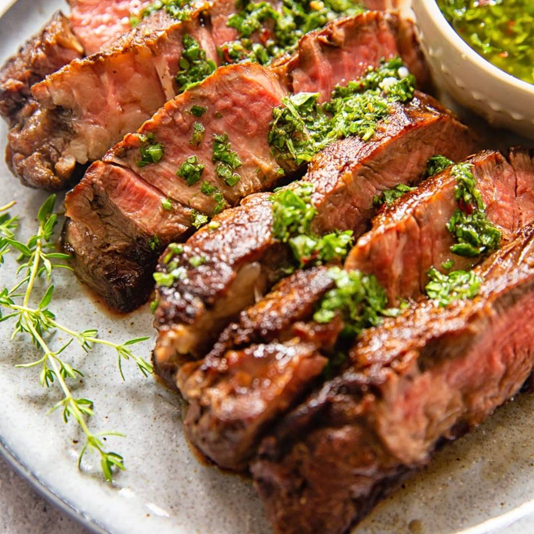 a sliced rib eye steak on a plate with a herby green sauce drizzled on top
