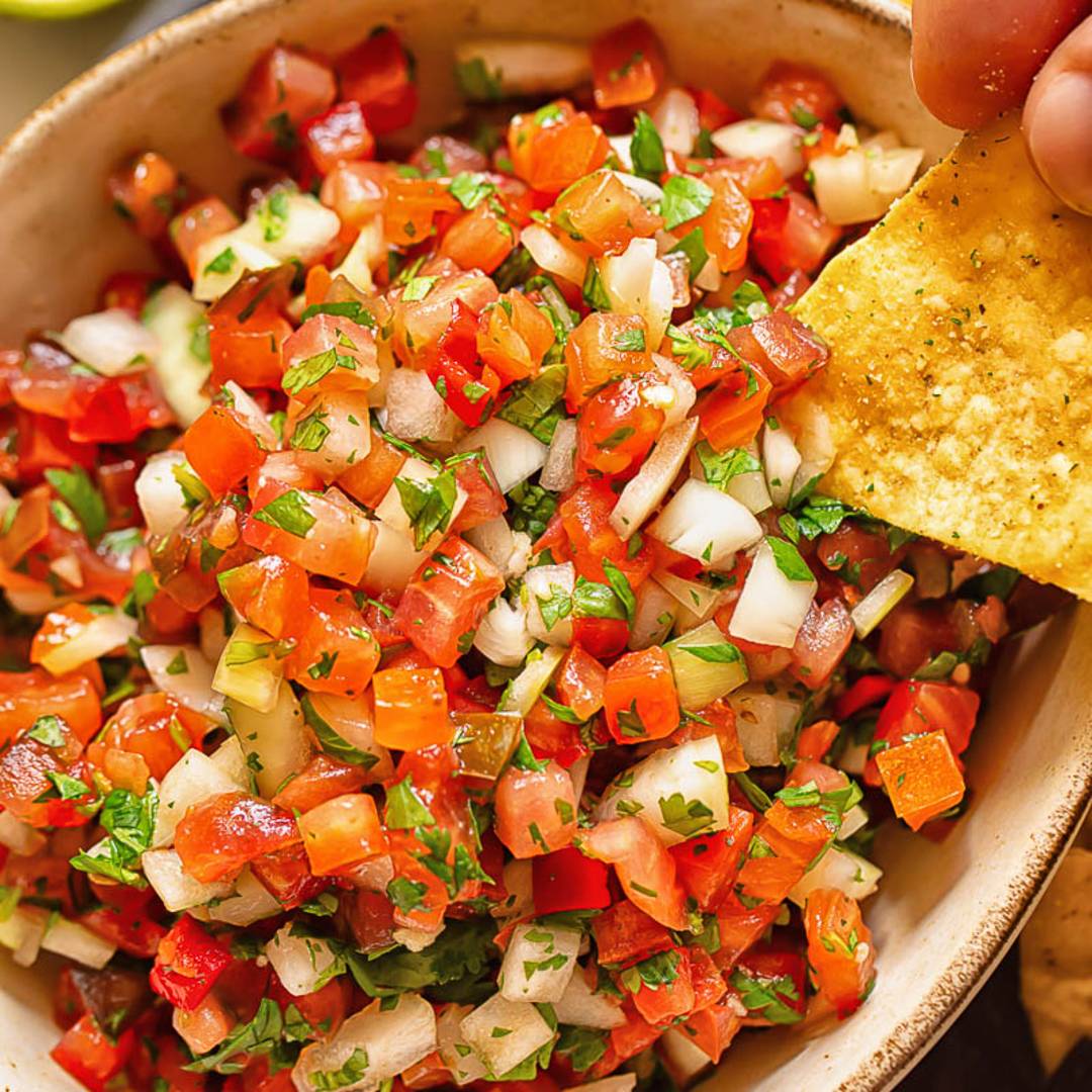 bowl of salsa with small pieces of tomato, onion and herbs with a hand holding a tortilla chip