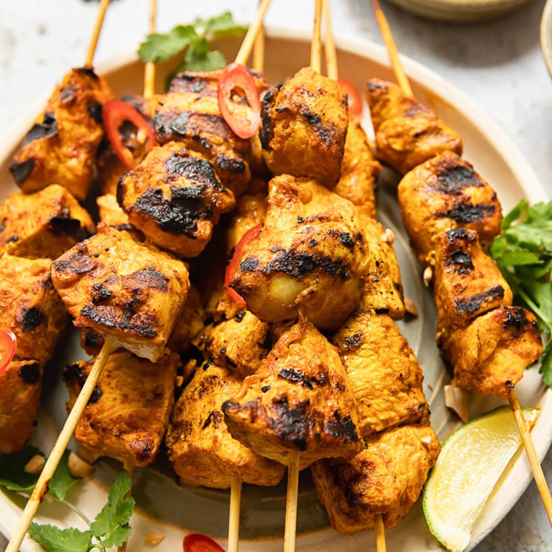 skewered chicken on a plate with peanut sauce in the background