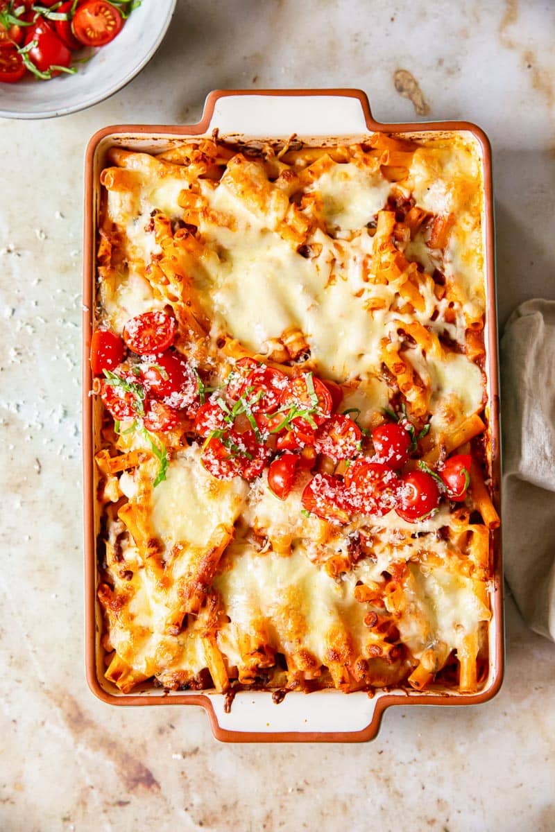 baked pasta covered with melted cheese in a baking dish, with extra topping of cherry tomatoes