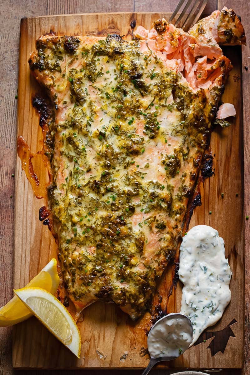 large slab of salmon on a wooden board, topped with greed spread and alongside lemon and yogurt