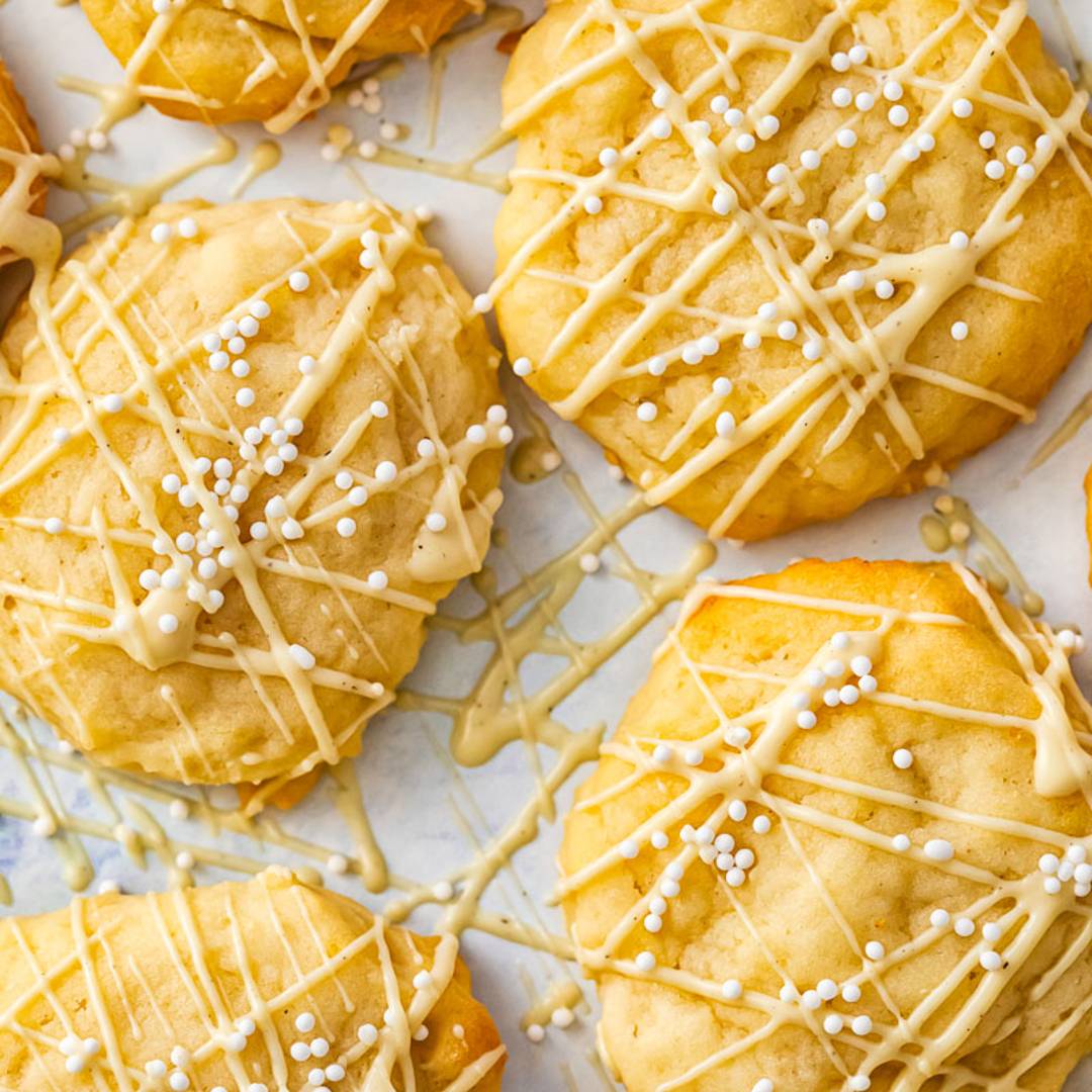 close up of a series of yellow cookies on a white background, with drizzle of icing and white beads