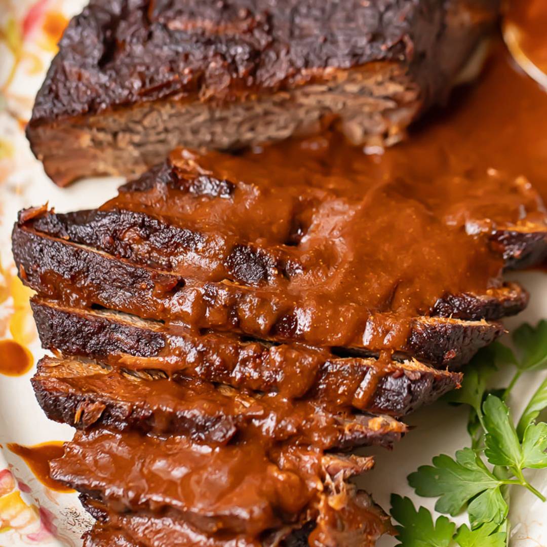 Beef brisket, half sliced, on a platter with gravy.